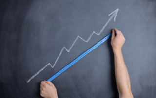 A chalkboard with an arrow drawn going upwards at an angle, with two arms holding a tape measurer up to the arrow
