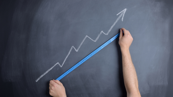 A chalkboard with an arrow drawn going upwards at an angle, with two arms holding a tape measurer up to the arrow
